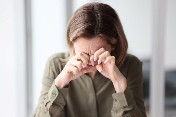 Mulher esfregando os olhos - sintoma de "olho seco" - uma das consequências da retração palpebral.