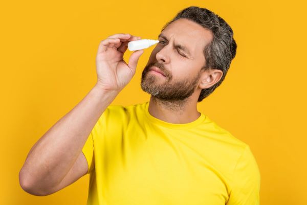 Homem maduro pingando colírio nos olhos - uma das formas de tratamento da retração palpebral.