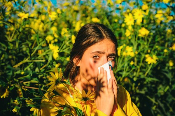 Jovem em meio a flores amarelas, assoando o nariz . A primavera e as alergias .