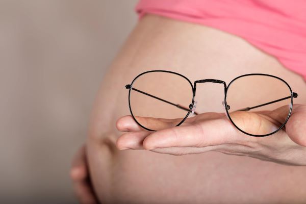 Mulher gravida segura um par de óculos frente à barriga.