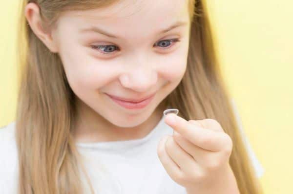 Menina loira observa uma lente de contato no dedo indicador.
