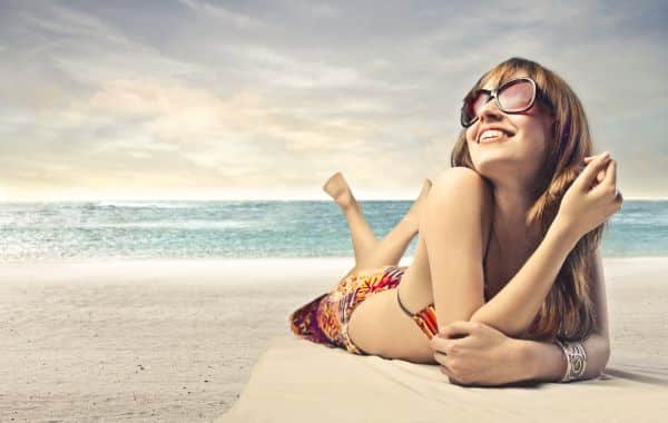 Jovem sorridente, deitada na areia da praia com o rosto voltado para o sol. aproveita a estação do calor: verão.