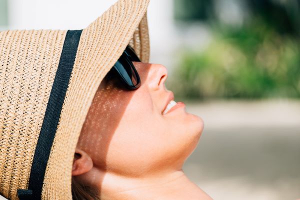Jovem mulher protege-se dos raios solares usando chapéu e óculos de sol escuros. Conceito de fotossensibilidade.