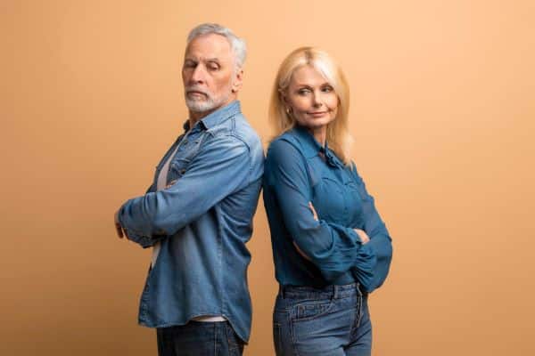 Homem grisalho e mulher de meia idade, vestindo roupas em jeans azul, de braços cruzados, em dúvida sobre qual dos gêneros tem maior predisposição ao glaucoma.