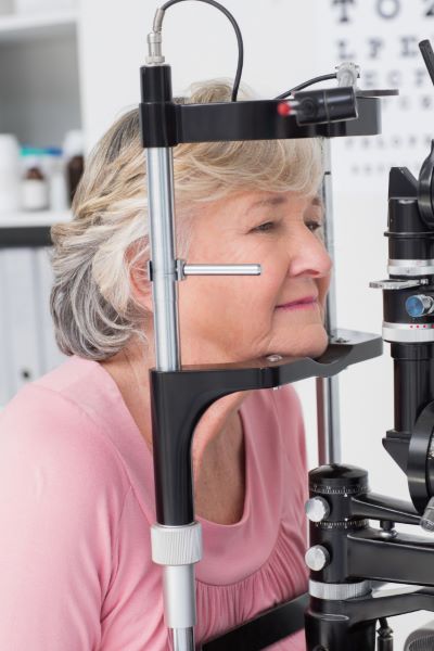 Paciente idosa, com cabelos grisalhos, vestindo blusa cor de rosa, realiza exame oftalmológico para detectar glaucoma.
