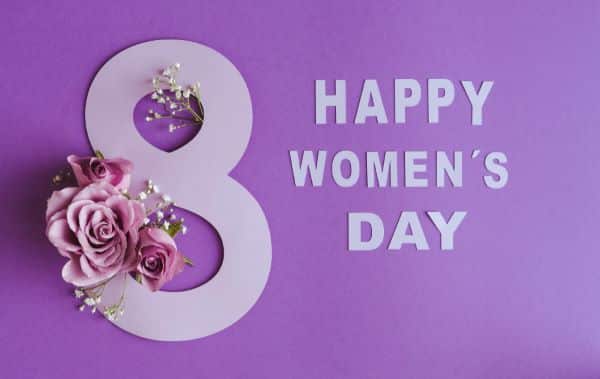 8 de março - Dia Internacional da Mulher . Imagem com rosas violetas sobre o número 8 e HAPPY WOMEN'S DAY escrito em letras de papel . 
