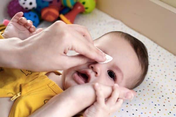 Mamãe limpando o olhinho de bebê que está com infecção nas vias lacrimais.