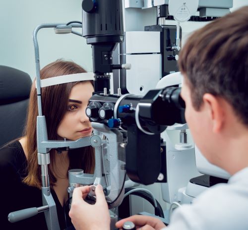 Jovem, com cabelos castanhos e vestindo uma blusa preta, faz avaliação oftalmológica em um instrumento ocular para verificar o pós-operatório.