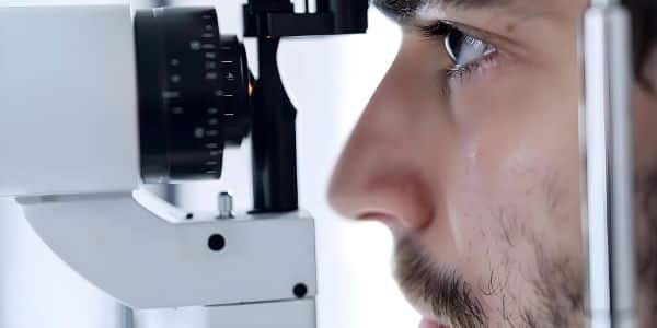 Homem jovem, com barba e bigode, está realizando exame oftalmológico para detectar erros refrativos.