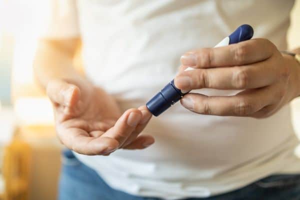 Jovem realizando exame de controle de diabete por meio de testagem com a caneta em um dos dedos da mão.