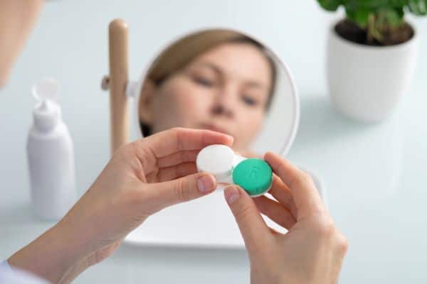 Uma mulher segura um recipiente para lentes de contato nas mãos com a intenção de realizar a higiene das mesmas.