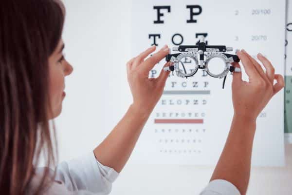 Médica oftalmologista segura em suas mãos um instrumento de avaliação oftalmológica frente ao teste de letras preso na parede.