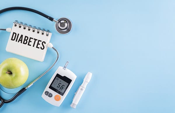 Aparelhos de medir glicose, estetoscópio, 1 maça verde e um bloco de anotações no qual está escrito "Diabetes".