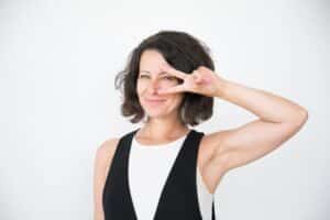 Mulher de meia idade, feliz, destaca a área dos olhos com a mão esquerda.