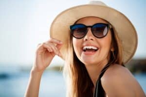 Linda jovem, usando óculos de sol e chapéu, aproveita o dia na praia.