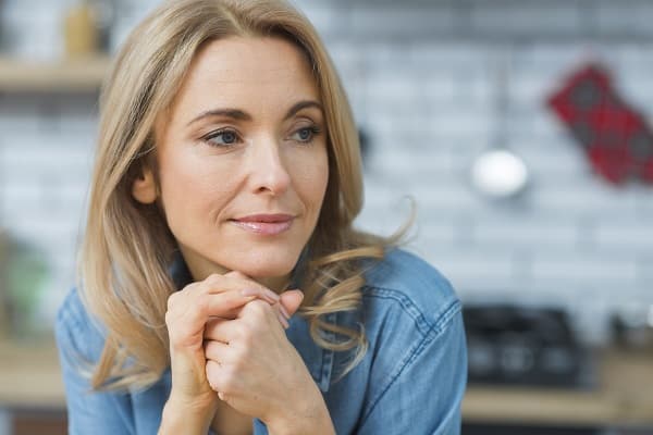 Mulher de meia idade, charmosa, vestindo camisa jeans, esboça um leve sorriso.
