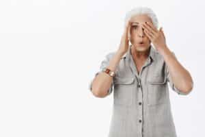 Charmosa senhora idosa com expressão de espanto cobrindo um dos olhos com a mão.