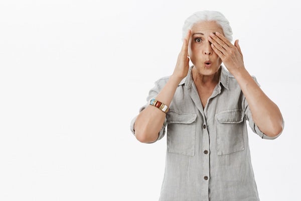 Charmosa senhora idosa com expressão de espanto cobrindo um dos olhos com a mão.