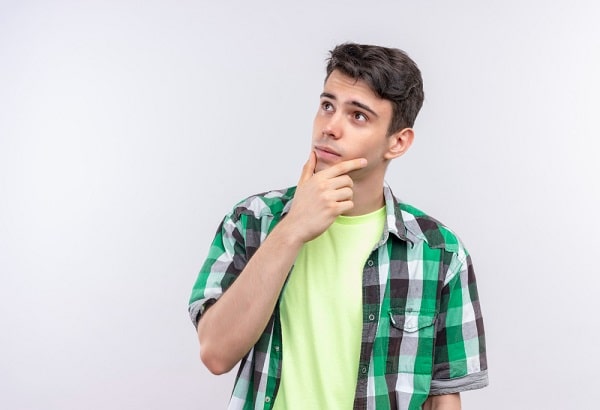 Lindo jovem, com a mão segurando o queixo, vestindo camiseta verde clara e sobre ela uma camisa xadrez , apresenta expressão de dúvida sobre o glaucoma em jovens.