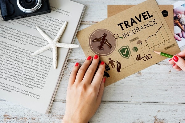 Sobre uma mesa, mãos femininas conferem um seguro viagem.