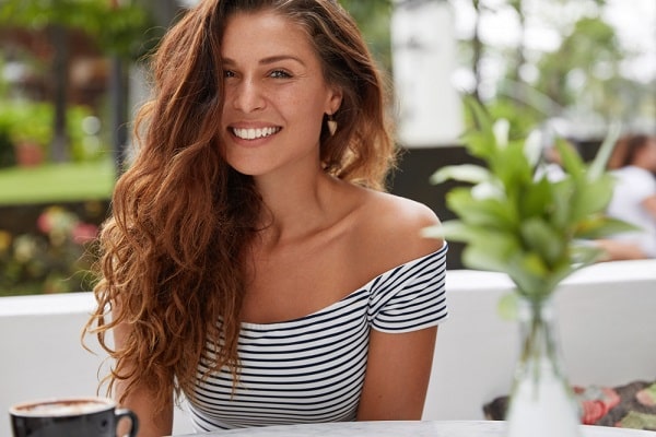 Mulher bonita e jovem, de cabelos longos e encaracolados, feliz, aproveitando o dia em um café.